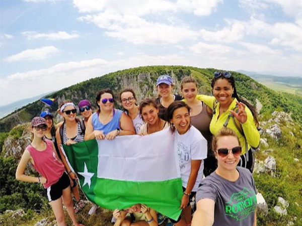 Group of UNT students studying abroad and holding a UNT flag on top of a mountain. 